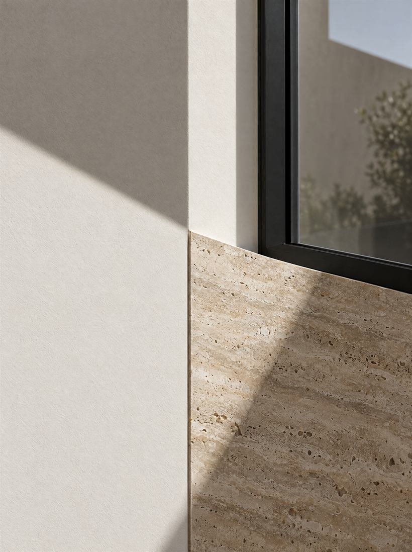 Encuentro entre pared blanca, panel de travertino y marco de ventana negro bajo luz diagonal
